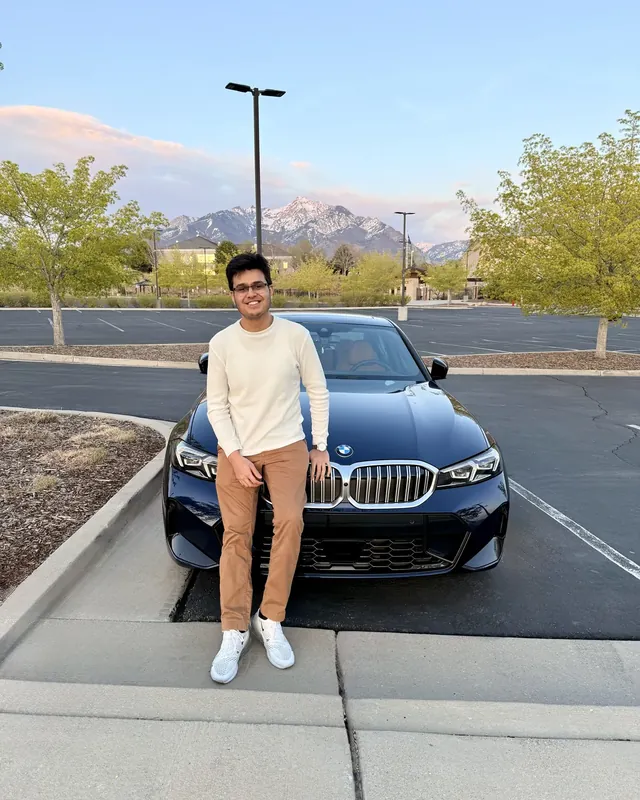 Drumin Gajjar in front of a navy BMW, snow-capped mountains in the background